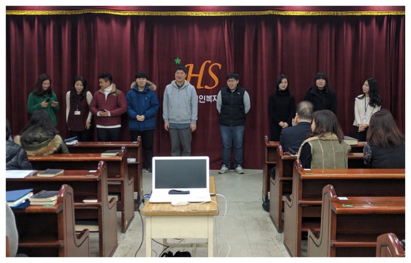9명의 복지관 직원들이 앞에 서서 새해의 덕담을 발표하고 있는 모습