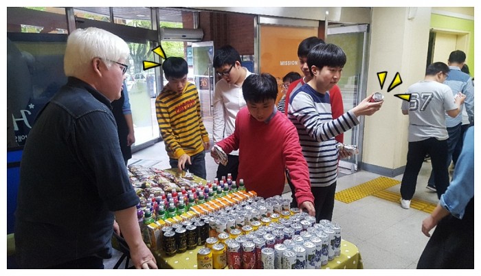 복지관 1층 안내실 앞에서 테이블에 음료수과 포장된 과자를 진열하고, 복지관 방문하는 이용인분들에게 나누어주고 있는 모습