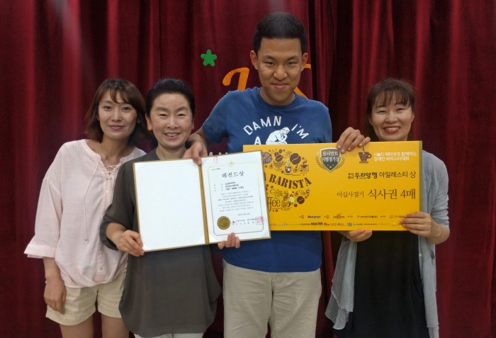 복지관 강당 앞에서 바리스타 수상을 한 조남영 바리스타와 하상직원이 상장과 상패를 들고 기념사진을 찍고 있는 모습