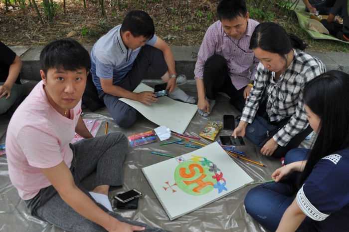 직원들이 둘러 앉아 스케치북에 그림을 그리고 있는 모습