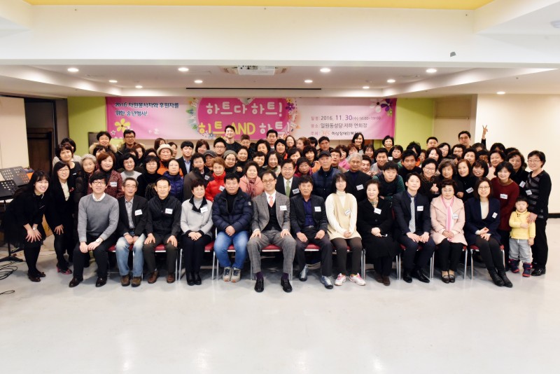 자원봉사자와 후원자를 위한 송년행사에 참여한 모든 사람들이 현수막을 배경으로 단체사진을 찍고 있는 모습