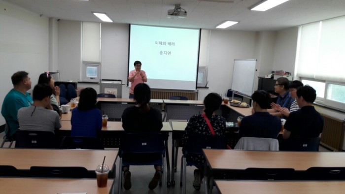 강의실에서 강연자가 의자에 앉은 청중들에게 이야기하고 있는 모습