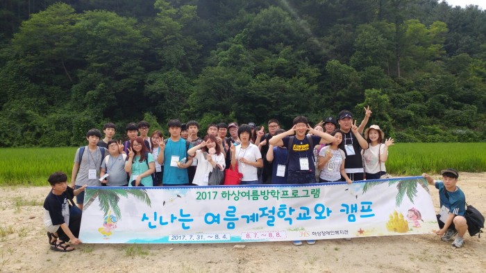 2017 여름계절학교와 캠프에 참여한 이용자, 직원, 봉사자들이 현수막을 들고 산을 배경으로 단체사진을 찍고 있는 모습