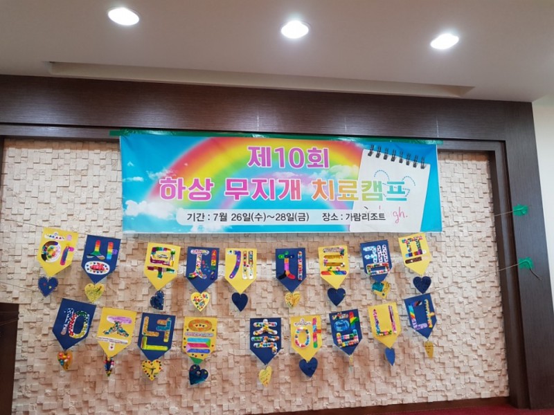 제10회 하상 무지개 치료캠프가 적혀있는 현수막과 하상 무지개 치료캠프 10주년을 축하합니다 글씨로 꾸며진 벽