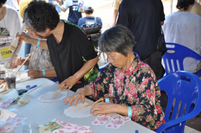 한지부채꾸미기부스에서 흰부채에 꽃모양으로 꾸미기를 하고 있는 참여자