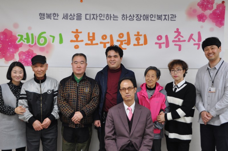 홍보위원과 복지관 직원들이 [홍보위원회 위촉식] 현수막을 배경으로 기념사진을 찍고 있는 모습