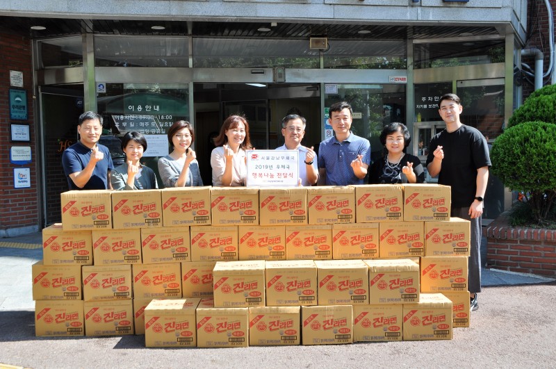복지관 현관에서 후원품 라면 45박스와 서울강남우체국 임직원 6명과 복지관 국장, 전략기획팀장이 함께 찍은 단체사진