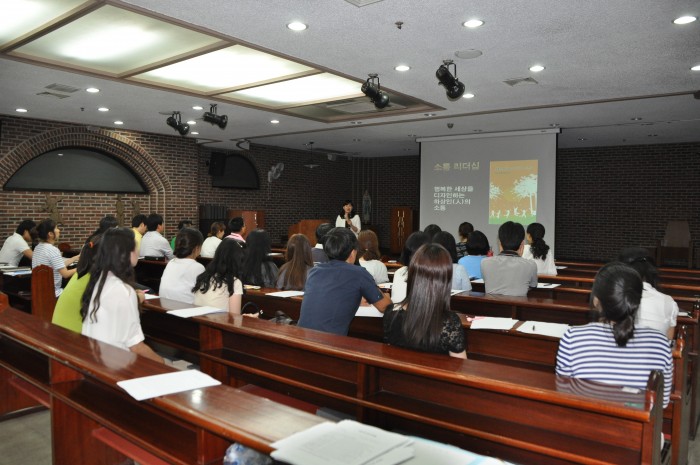 지하 강당에서 정윤희 강사님께서 소통에 대해 파워포인트를 활용하여 강의하고 계시고, 직원 50여명이 강의를 듣고 있는 모습입니다.